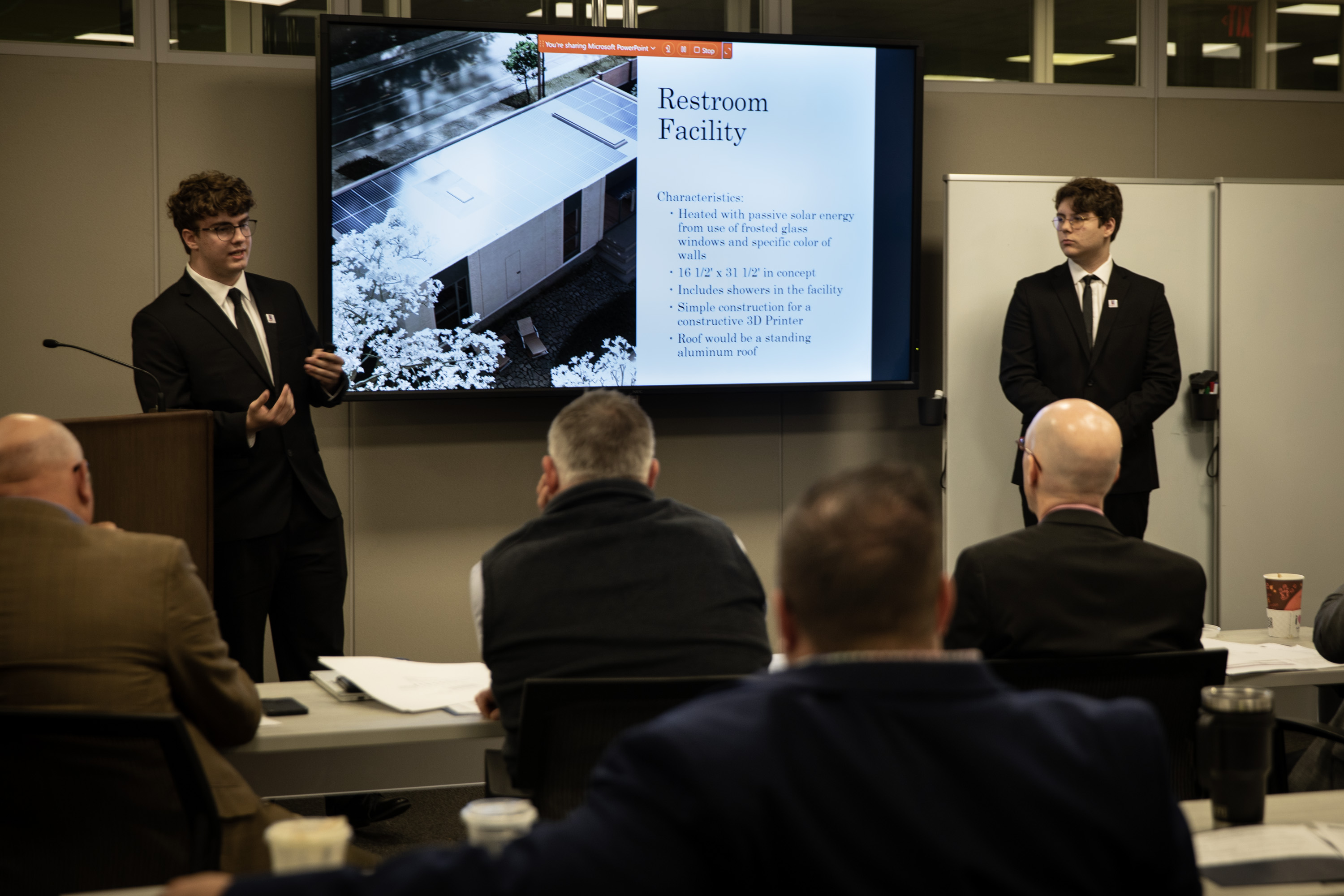 Elijah Mumau and Robert John, the team from Lenape Technical School, standing at the front of a room presenting to the PennDOT Secretary and a panel of judges with a screen behind them showing their PowerPoint presentation